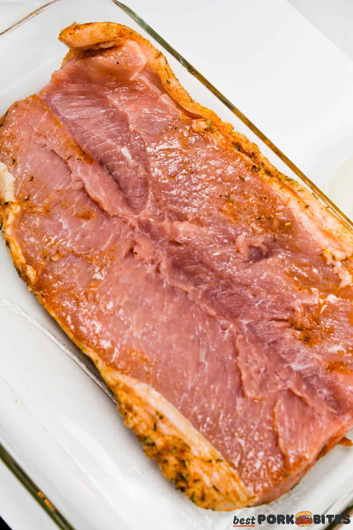 sliced open and seasoned raw pork tenderloin in a baking dish